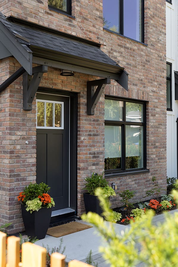 Townhome exterior at Rindall Port Coquitlam featuring red brick faรงade, black front door, covered entry, and landscaped front yard by Woodbridge Homes at 2150 Rindall Avenue.